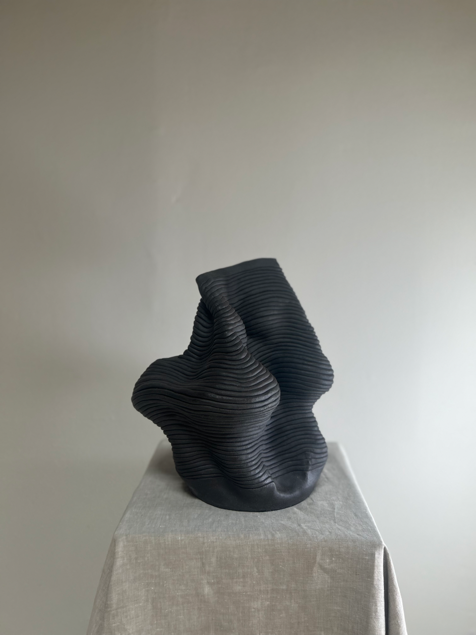 Black abstract sculpture on a gray pedestal against a plain background
