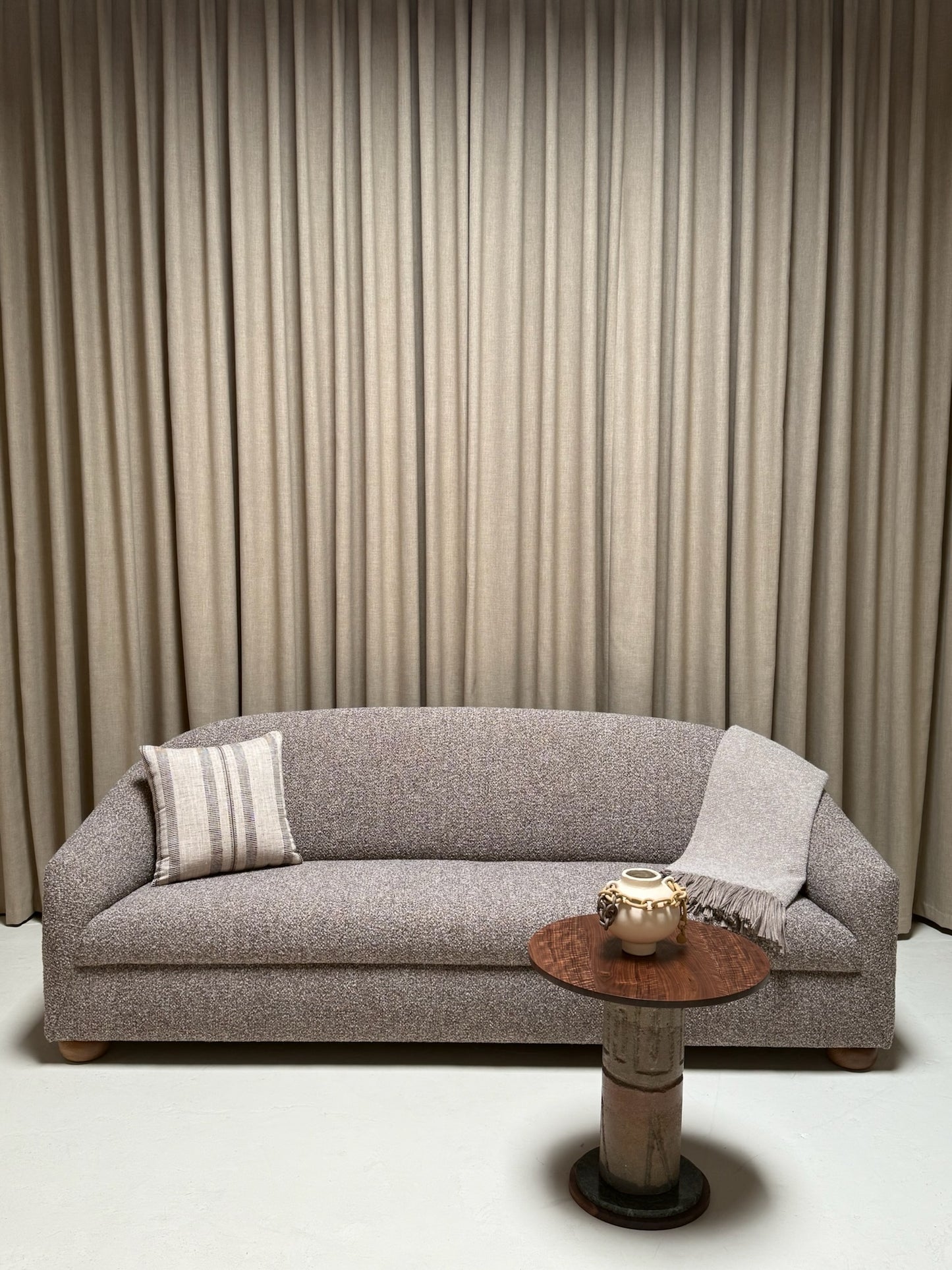 Gray sofa with a small round table against a beige curtain backdrop