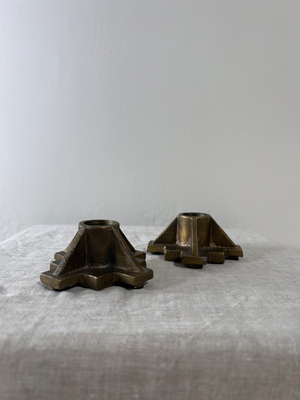 Two bronze candle holders on a textured surface with a plain background