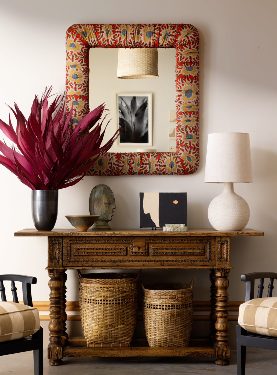 A rectangular mirror with a floral patterned wall behind it, complemented by a classic upholstered frame in a wood finish.