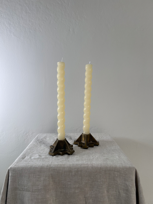 Two twisted candles in decorative holders on a gray surface with a gray background