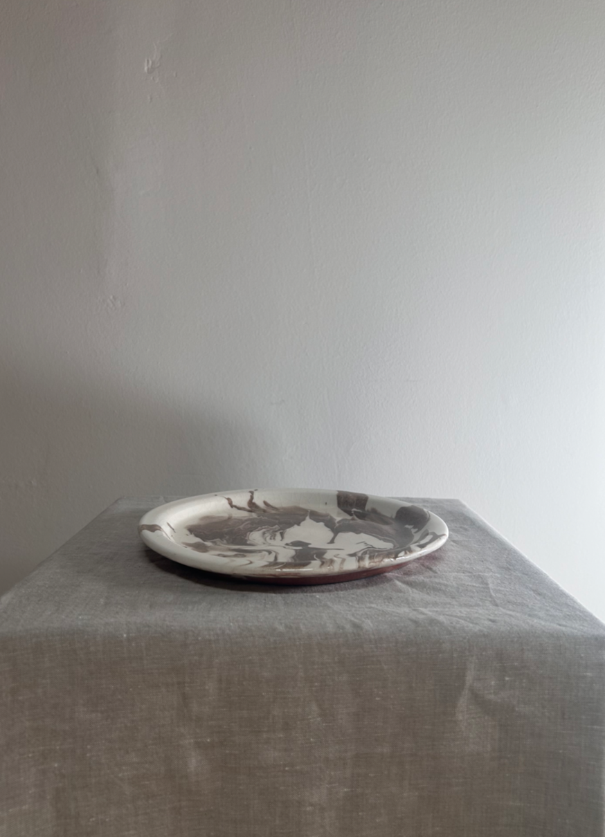Platter with a black and white design on a gray tablecloth against a plain wall