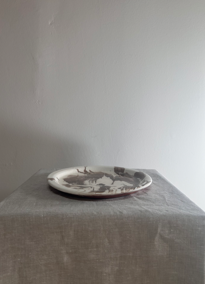 Platter with a black and white design on a gray tablecloth against a plain wall