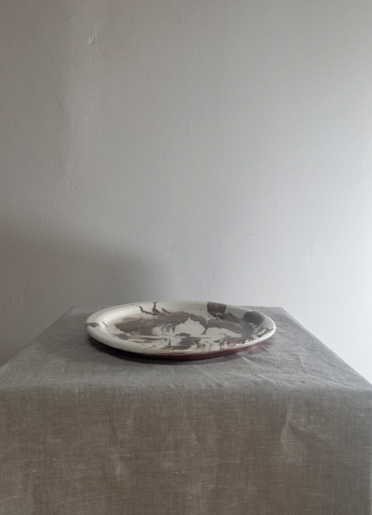 Platter with a black and white design on a gray tablecloth against a plain wall