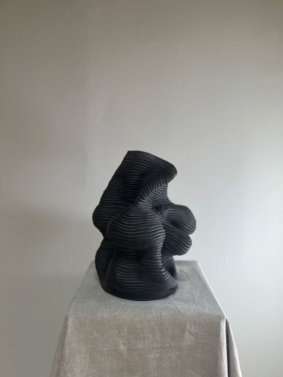Black abstract sculpture on a gray pedestal against a plain background