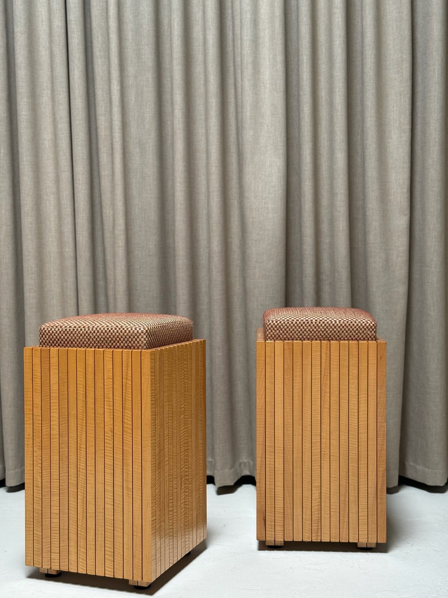 Two wooden stools with woven seats against a gray curtain background