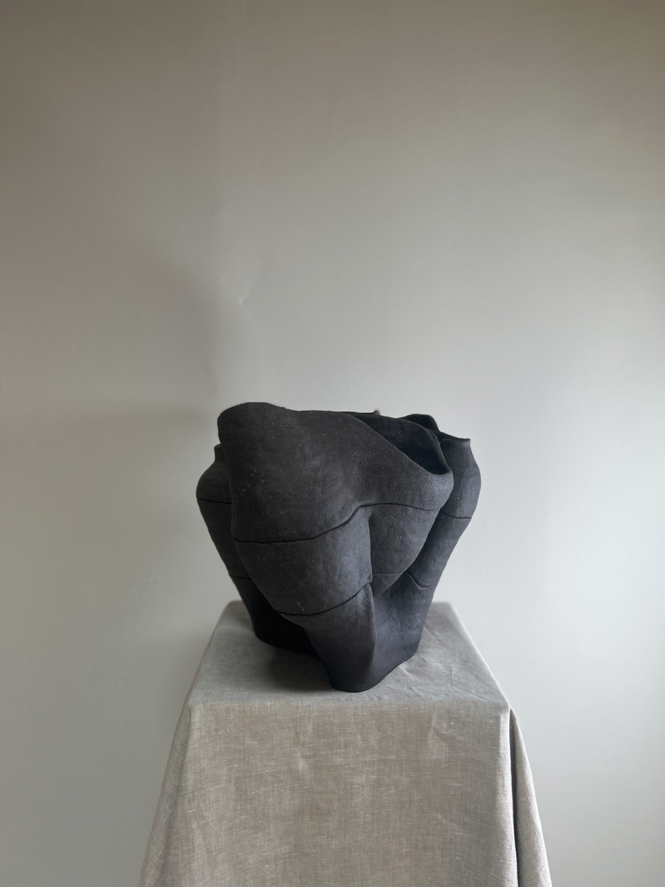 Dark gray ceramic sculpture on a light gray surface with a plain background