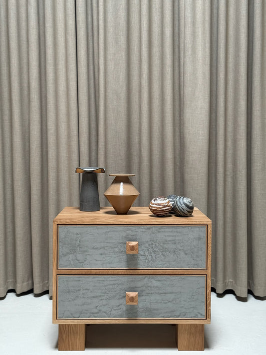 Wooden nightstand with gray drawers and decorative vases against a beige curtain background