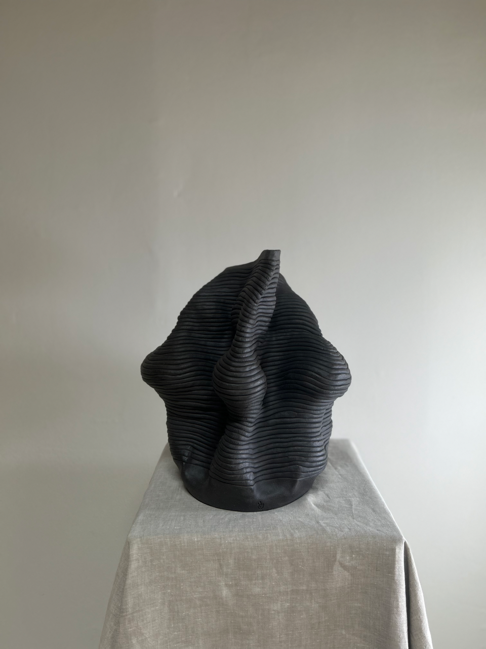 Black abstract sculpture on a gray pedestal against a plain background