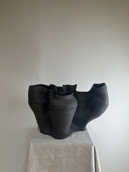 Black ceramic vase with ruffled edges on a light gray surface against a plain background