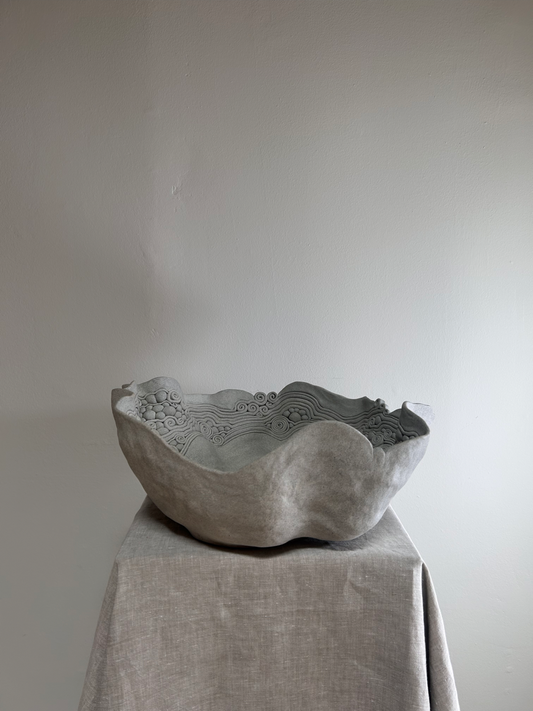 Decorative stone bowl on a draped fabric surface with a plain background