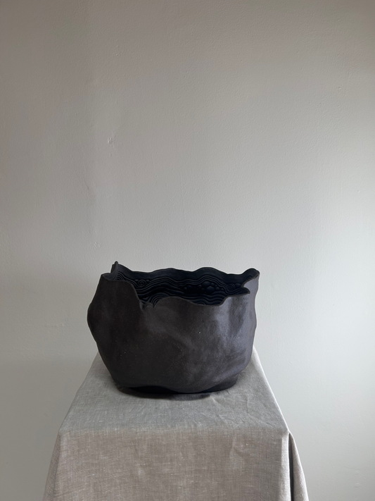 Black woven basket on a light gray surface with a plain white background