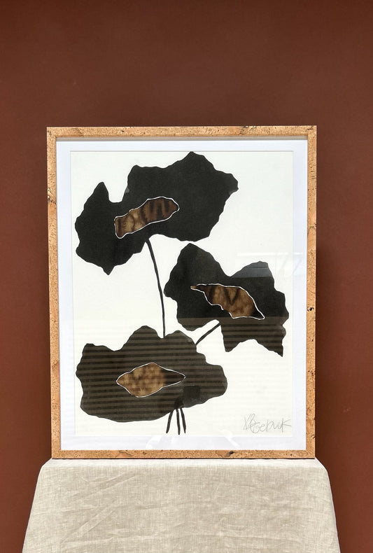 Framed artwork with abstract black and brown leaf-like shapes on a white background, against a brown wall.