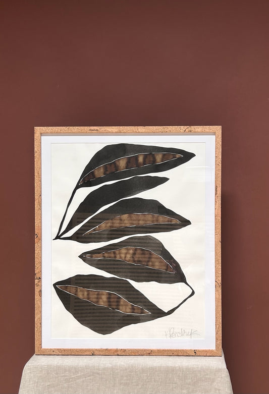 Framed artwork with black leaf shapes on a white background against a brown wall.