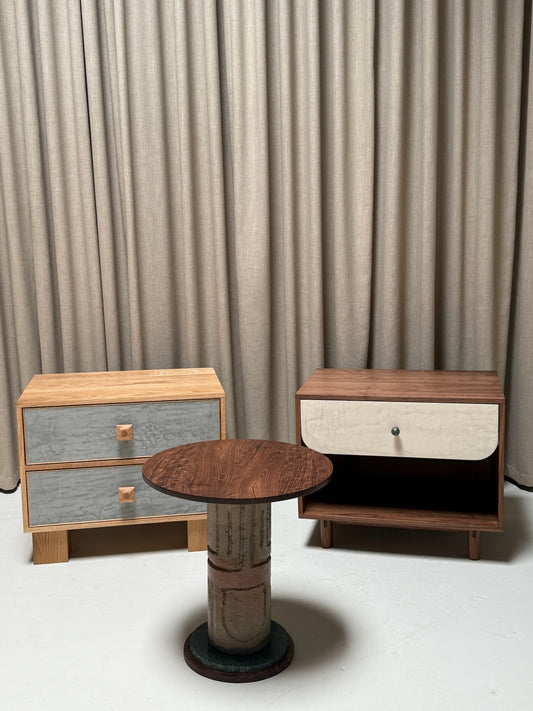 Two wooden nightstands with a round table in front against a gray curtain background