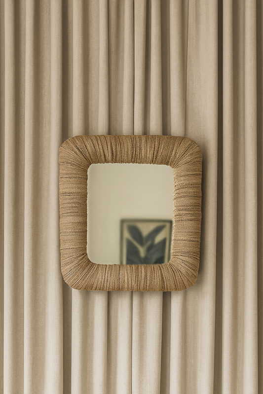 A small rectangular mirror with a beige upholstered frame, woven pattern design, reflecting a portion of a room in the mirror's frame.