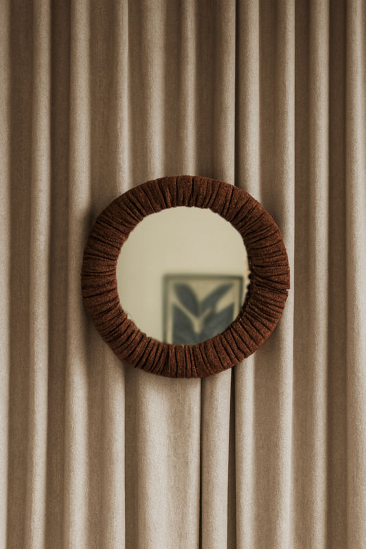 Round mirror with a brown frame on a beige curtain