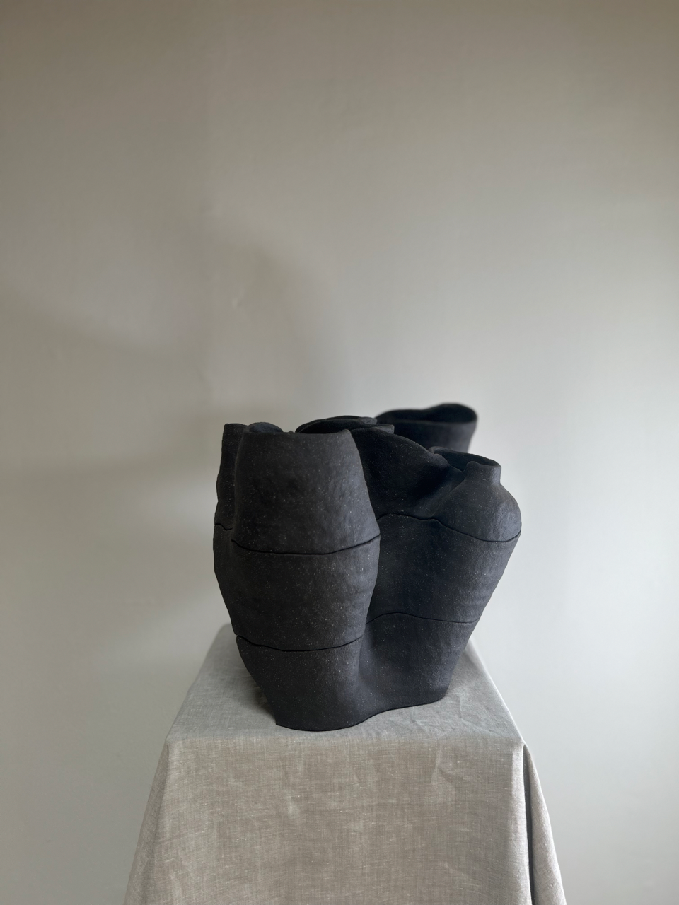 Two black ceramic vases on a textured surface with a plain background
