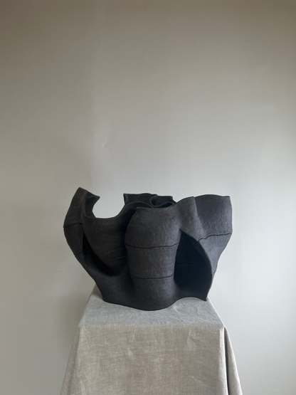 Black ceramic sculpture on a gray pedestal against a plain background
